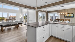 A modern kitchen with white cabinetry, a large island, pendant lighting, and a view of the outdoors. - New! Luxe Sandbridge Beach, Pool, Hot Tub (Virginia Beach)