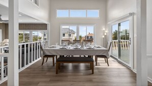 A dining area with a table set for four, large windows, and a view of the outside. - New! Luxe Sandbridge Beach, Pool, Hot Tub (Virginia Beach)
