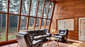 A spacious room with large windows, a leather sofa, a leather armchair, and a glass coffee table. - Unique Durham Cabin with Hot tub and close to Duke (Durham)