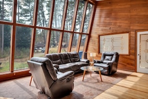 A spacious room with large windows, a leather sofa, a leather armchair, and a glass coffee table. - Unique Durham Cabin with Hot tub and close to Duke (Durham)