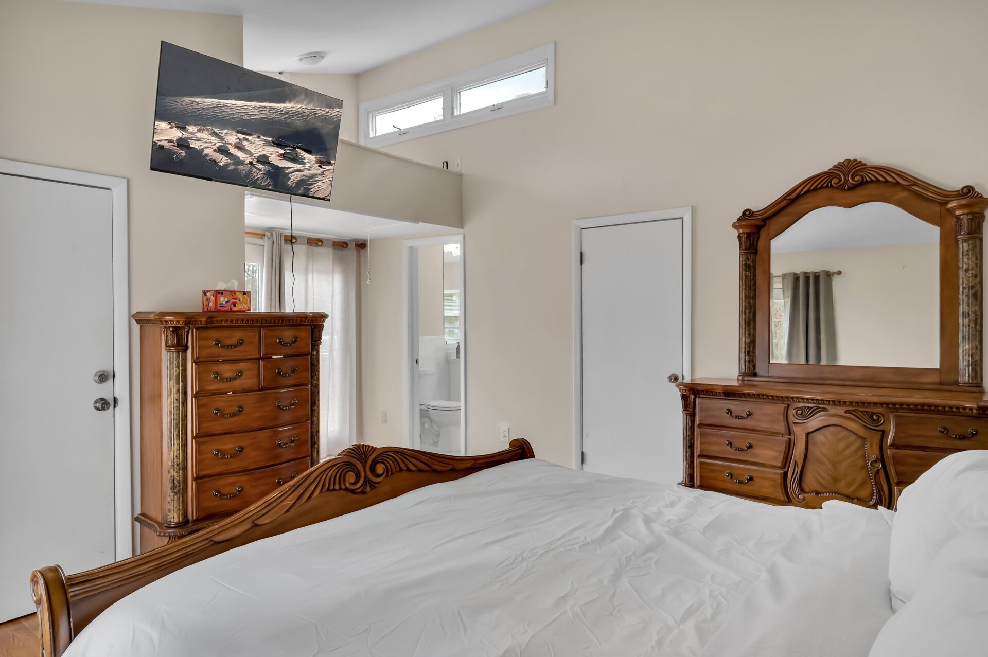 Een slaapkamer met een groot bed, een houten dressoir, een spiegel en een tv aan de muur.