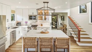 Une cuisine moderne dotée d’un îlot central, d’appareils électroménagers en acier inoxydable et d’un escalier en bois.