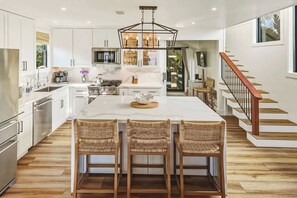 A modern kitchen with a central island, stainless steel appliances, and a wooden staircase. - Law St Sunset I Ocean Views , Outdoor Living (San Diego)