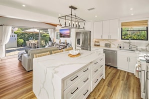 A modern kitchen with a marble island, stainless steel appliances, and a dining area with a view. - Law St Sunset I Ocean Views , Outdoor Living (San Diego)