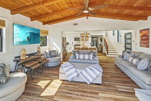A spacious living area with a wooden ceiling, a large TV, and a kitchen in the background. - Law St Sunset I Ocean Views , Outdoor Living (San Diego)