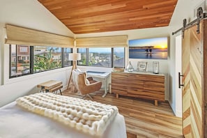 A bedroom with a bed, a desk, a chair, a dresser, and a large window with a view of the ocean. - Law St Sunset I Ocean Views , Outdoor Living (San Diego)