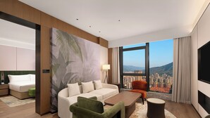 Ett modernt hotellrum med ett stort fönster, en soffa, en grön fåtölj, ett soffbord och en tv.