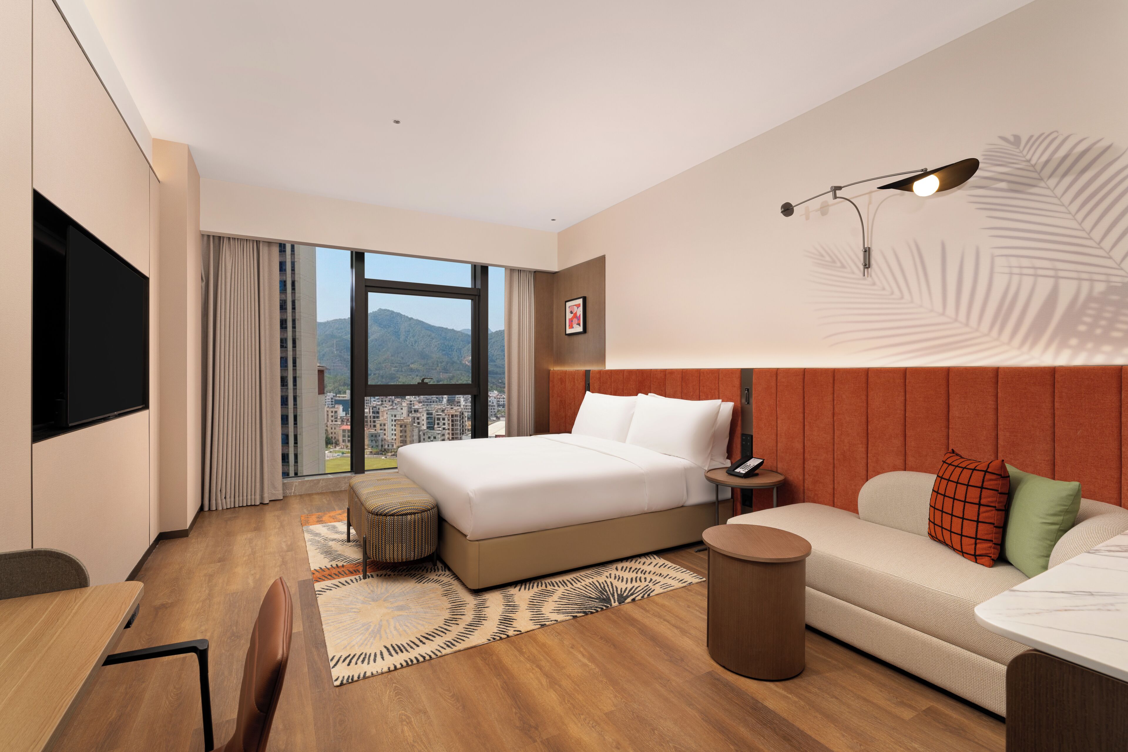 A modern hotel room with a large bed, a sofa, a small table, and a TV.