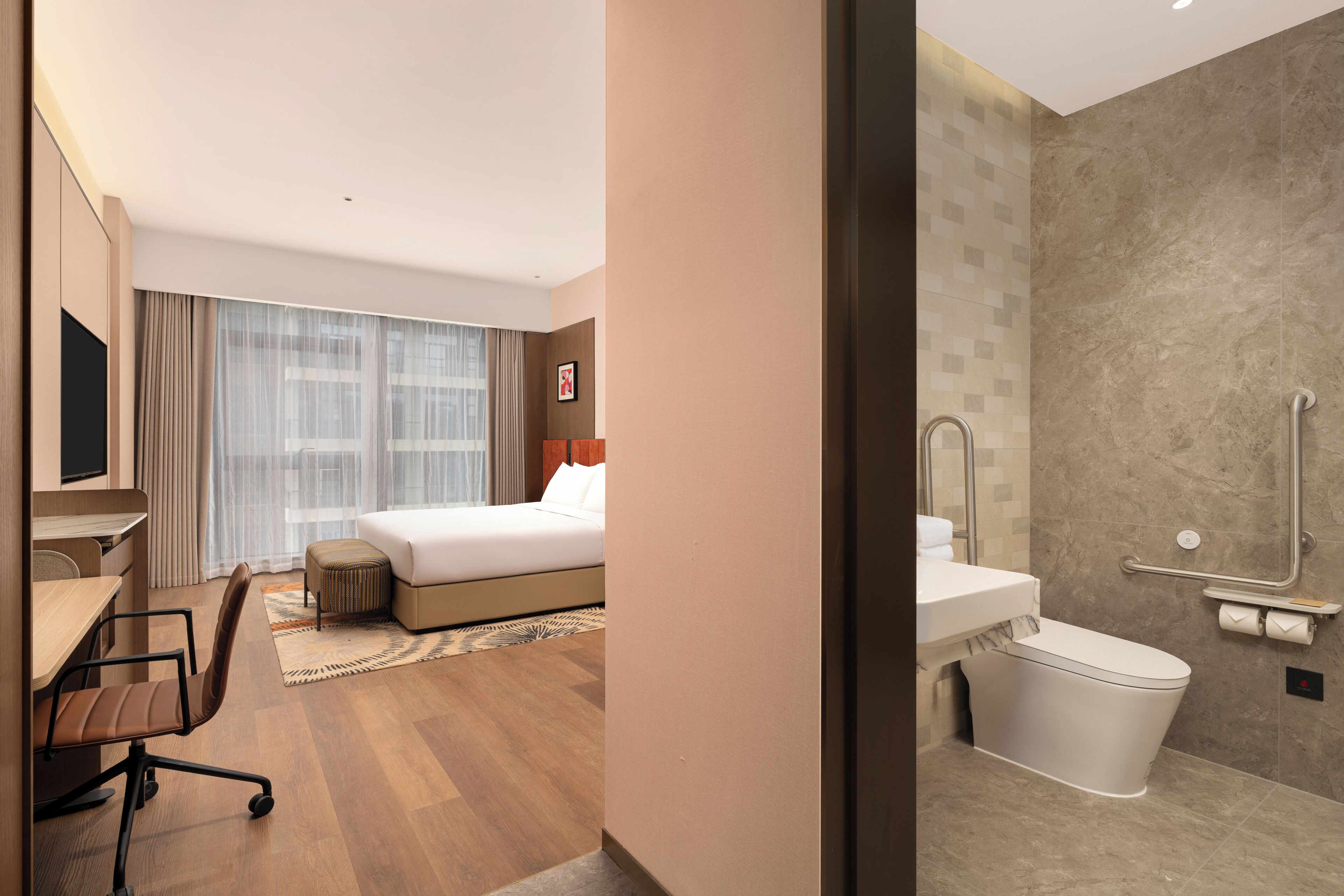 A hotel room with a bed, desk, chair, and a bathroom with a toilet and shower.