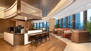En modern hotellobby med en central ö, en sittgrupp och stora fönster med utsikt över staden.