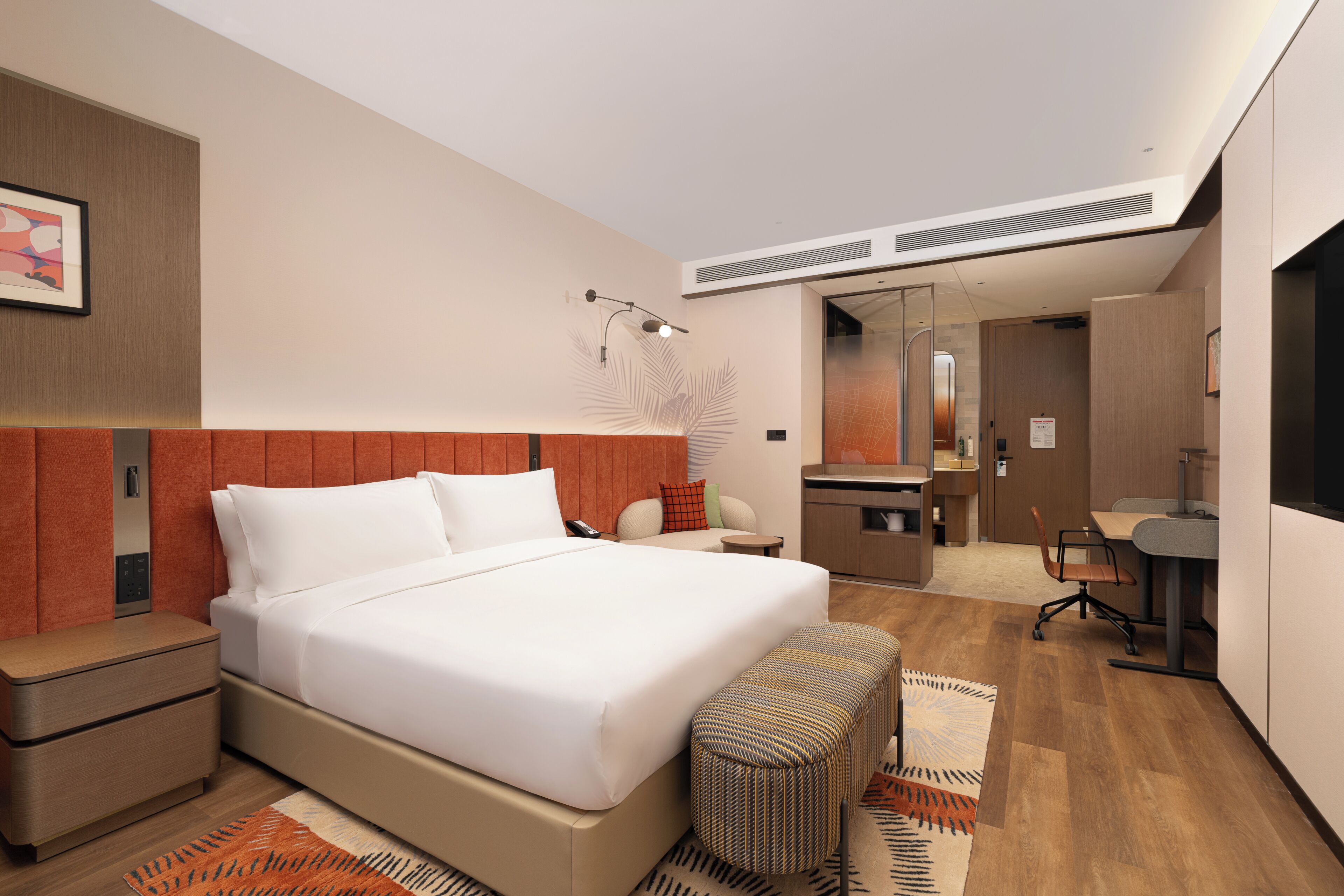 Una habitación de hotel moderna con una cama grande, un escritorio, una silla, una mesita, un banco y un espejo.
