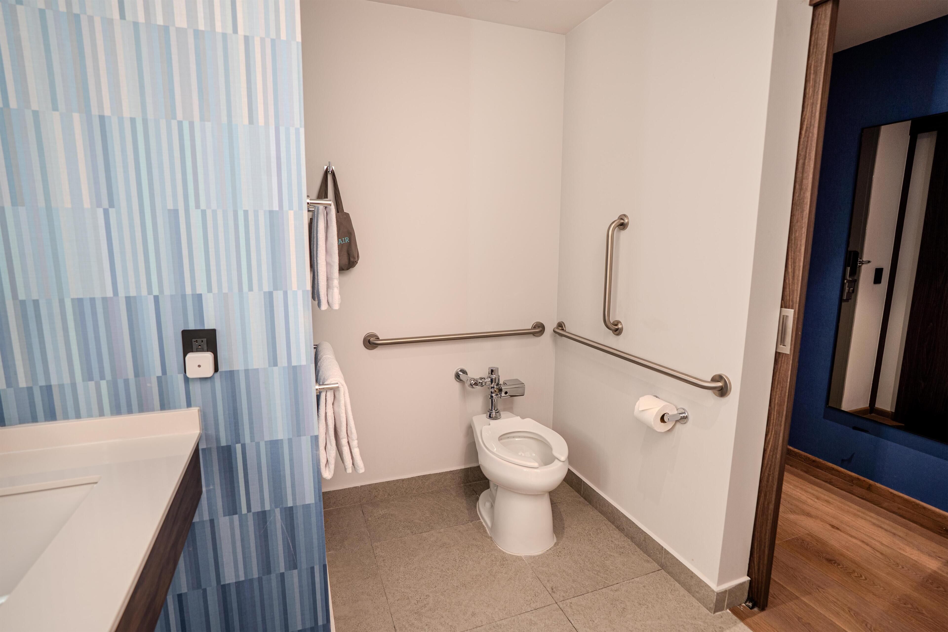 A bathroom with a toilet, handrails, a towel rack, and a sink.