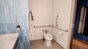 A bathroom with a toilet, handrails, a towel rack, and a sink.