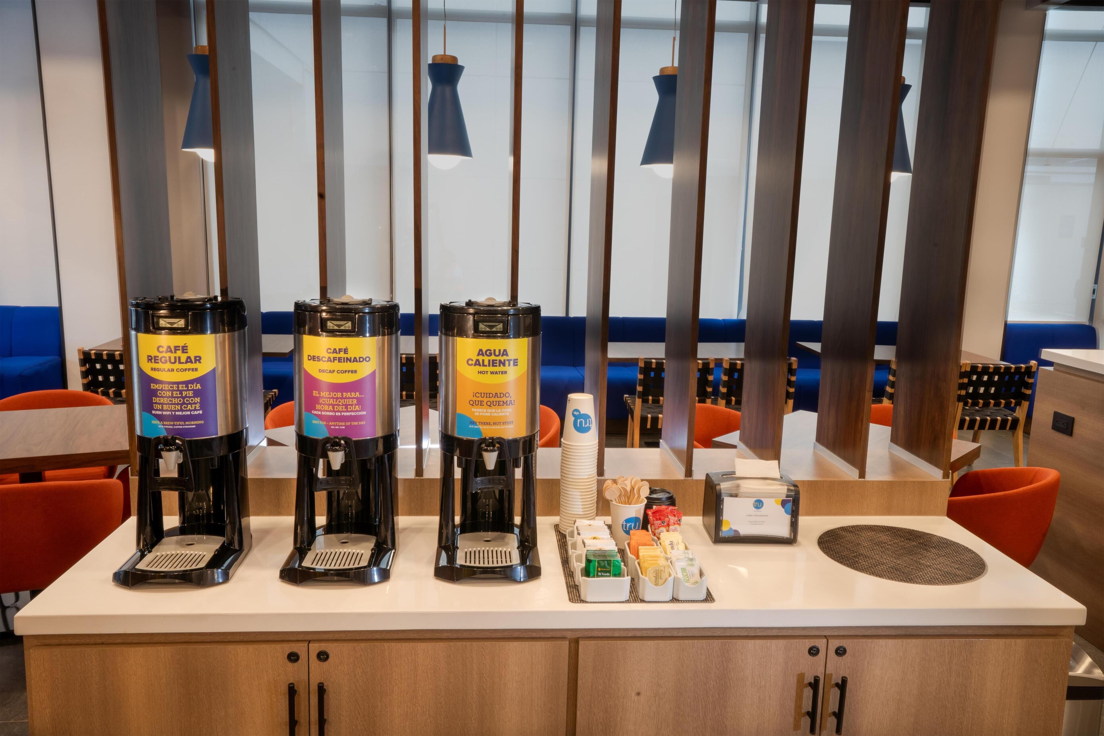 Un espace dédié au café, équipé de trois distributeurs de café étiquetés « CAFÉ NORMAL », « CAFÉ DÉCAFÉINÉ » et « EAU CHAUDE ».
