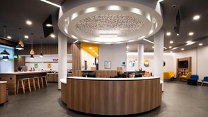 Un espace d’accueil moderne doté d’un comptoir central, de plusieurs options d’assises et d’un plafond haut avec des luminaires encastrés.