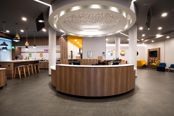 Een modern receptiegebied met een centraal balie, diverse zitmogelijkheden en een hoge plafond met ingebouwde verlichting.