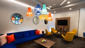 Un espace de détente moderne avec un canapé bleu, des fauteuils jaunes, une table basse et des lampes suspendues aux couleurs vives.