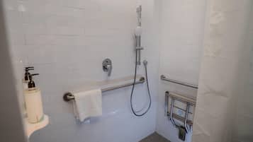 A bathroom with white tiled walls, a shower with a handheld showerhead, a towel rack, and a soap dispenser.