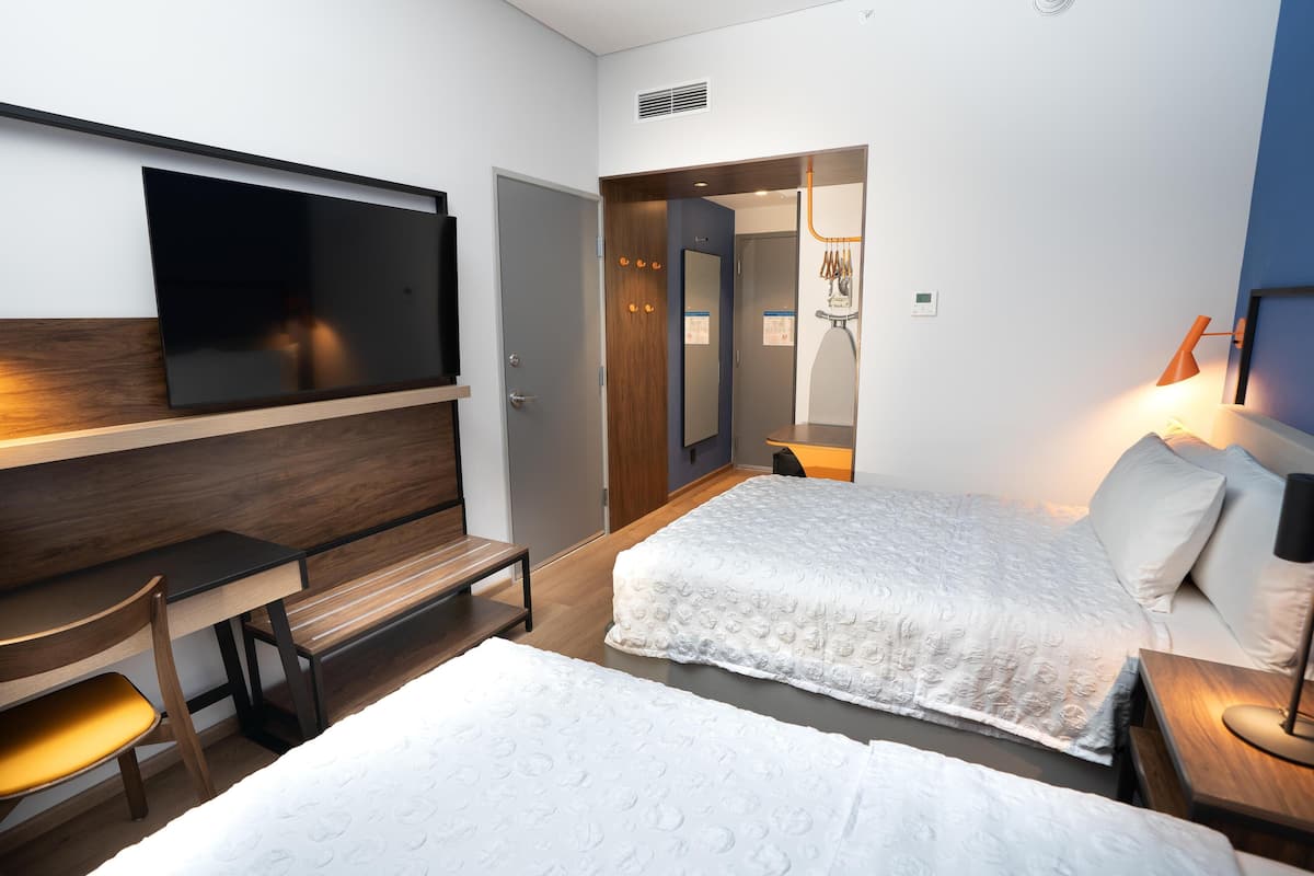 Una habitación de hotel con cama, escritorio, silla, televisor y lámpara.