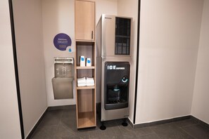 Ein Wasserspender, ein Getränkespender und ein Regal mit gefalteten Handtüchern in einem Hotelzimmer.