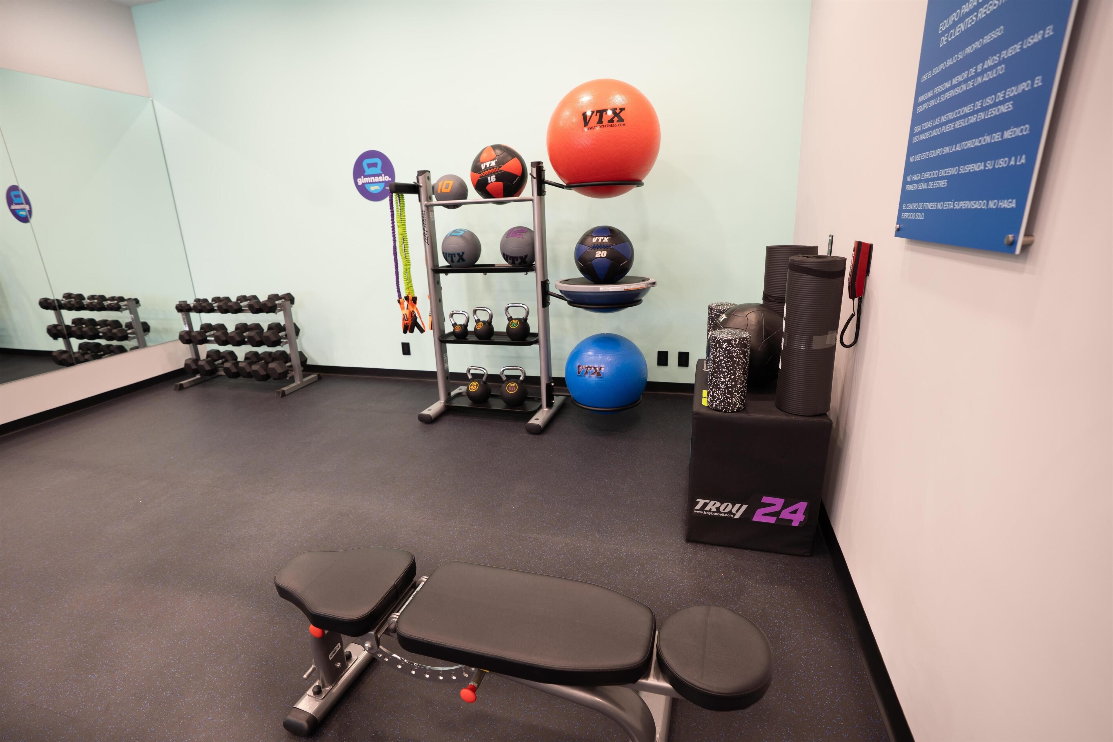 A gym with exercise equipment, a bench, dumbbells, and a wall with a sign.