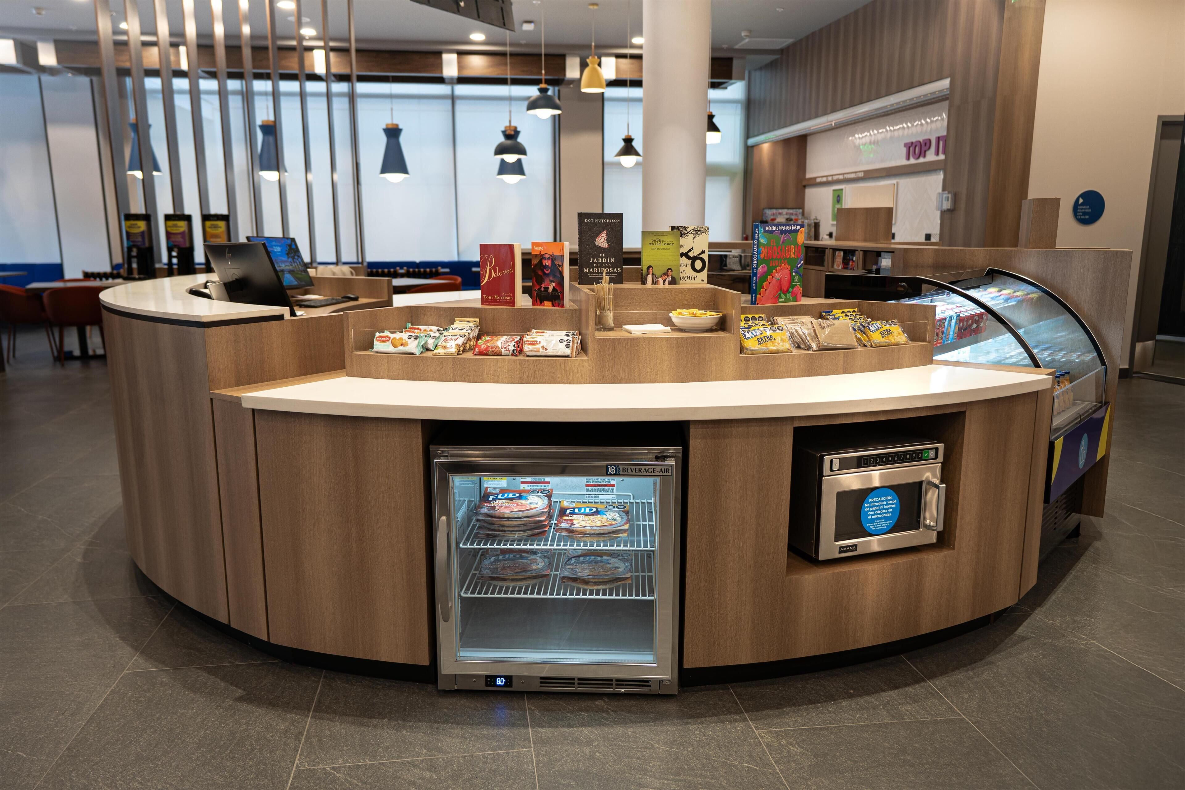Una moderna zona de recepción con mostrador curvo, vitrina refrigerada y máquina de café.