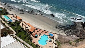 Vista aérea de um resort na praia, com piscina, espreguiçadeiras e costa rochosa.