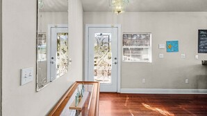 Una habitación con piso de madera, un candelabro, una puerta con un panel de vidrio decorativo y un letrero en la pared.