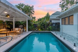 A swimming pool with a covered seating area, surrounded by lush greenery and a clear sky. - Luxury 4BR Villa | Resort Pool | Steps to Beach (Palm Cove)