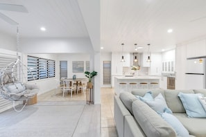 A modern kitchen with white cabinets, a dining area with a table and chairs, and a living room with a sofa. - Luxury 4BR Villa | Resort Pool | Steps to Beach (Palm Cove)
