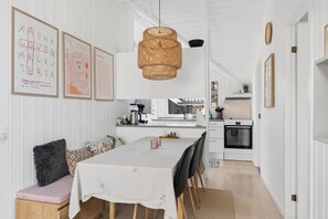A modern kitchen with white cabinetry, a dining area with a table and chairs, and a hanging woven light fixture. - Lovely cottage – close to a beautiful beach (Vig)