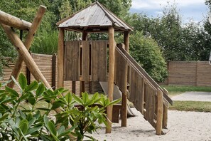 A wooden play structure with a slide and climbing area, surrounded by greenery. - Lovely cottage close to a beautiful beach (Vig)