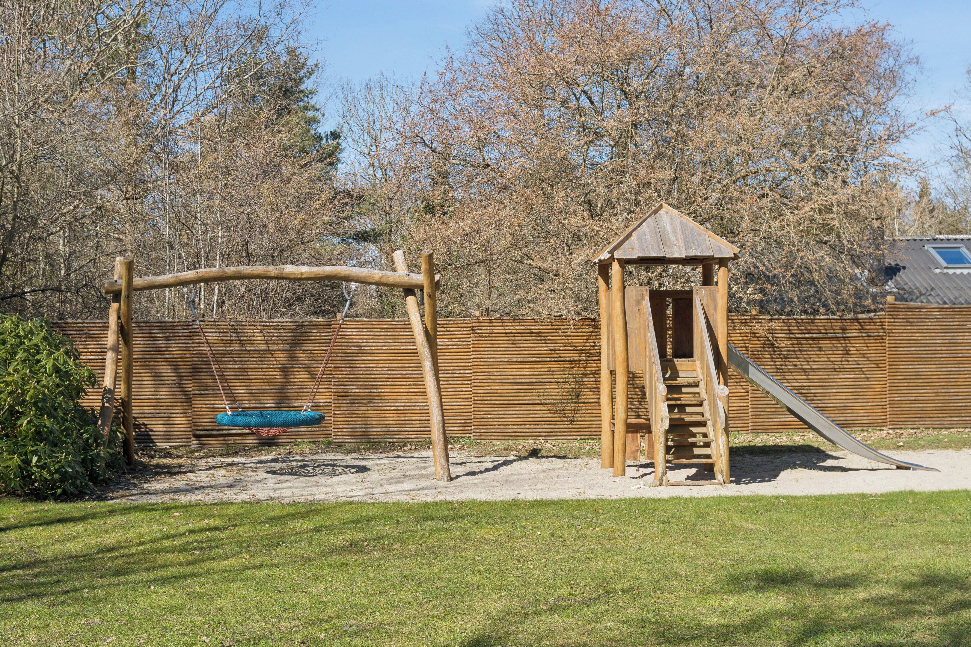 Un parque infantil con columpios, un tobogán y una pequeña estructura de madera.