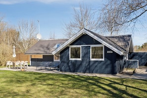 A single-story building with a dark exterior, a visible number '203b' on the side, a satellite dish, and a small patio area with outdoor furniture. - Lovely cottage close to a beautiful beach (Vig)