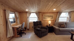 Et hyggeligt værelse med trævægge og -loft, et skrivebord med en computer, en behagelig lænestol, en sofa og en lampe.