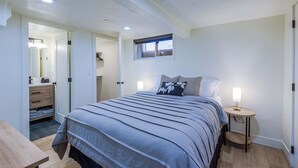 Een slaapkamer met een bed, nachtkastje, raam en een deur naar een badkamer.