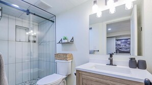 Een moderne badkamer met een douchecabine van glas, een wit toilet, een houten wastafelmeubel en een grote spiegel.