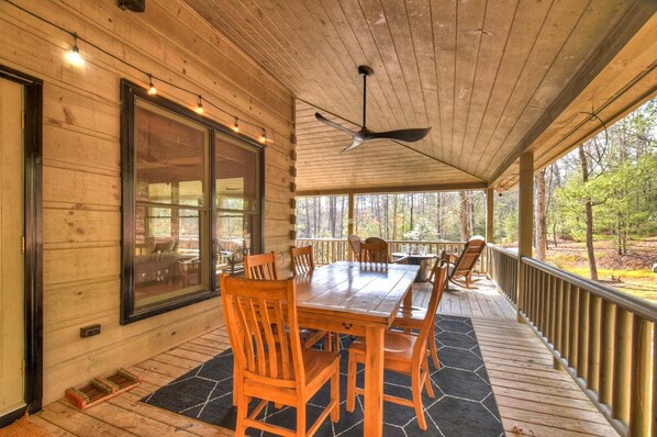 A wooden deck with a table and chairs, a ceiling fan, and a view of the forest. - Kick Aska Lodge・Hot Tub・Firepit・Game Room・Secluded (Cherry Log)