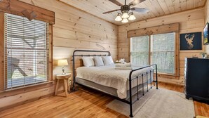 Camera da letto con rivestimento in legno, un letto, un comodino, una lampada e una ventola a soffitto.