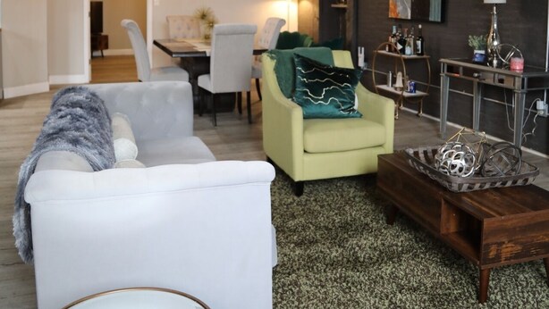 A modern living room with a white sofa, a green armchair, a wooden coffee table, and a dining area in the background. - Elevated Urban Living in Downtown St. Louis (St. Louis)