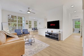 Een moderne woonkamer met een flatscreen televisie, een bank, stoelen, een eethoek en een plafondventilator.