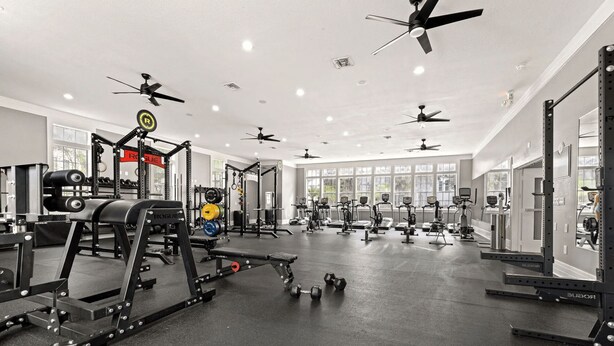 Een sportschool met plafondventilatoren, gewichthefapparatuur, loopbanden en hometrainers.