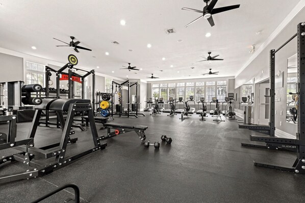 Une salle de sport équipée de ventilateurs de plafond, de matériel de musculation, de tapis de course et de vélos d’exercice.