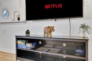 Un salon avec un téléviseur affichant le logo « NETFLIX », une figurine d’ours sur une étagère et une plante.
