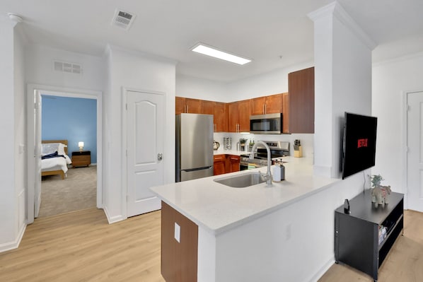 Una cocina moderna con armarios de madera, electrodomésticos de acero inoxidable, una isla integrada con fregadero y un televisor de pantalla plana montado en la pared.