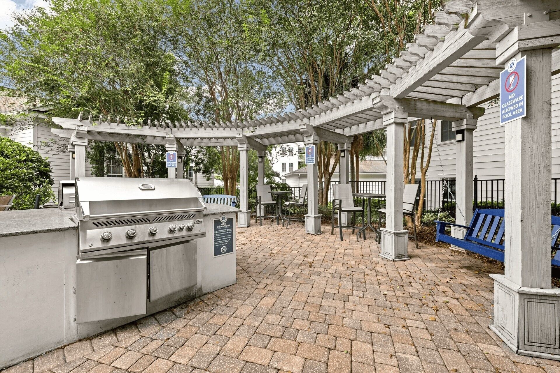 An outdoor patio with a grill, seating area, and a pergola structure.
