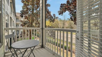 A balcony with a table and chairs, a railing, and a view of trees and a road.