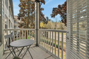 Un balcon avec une table et des chaises, une balustrade, et une vue sur des arbres et une route.