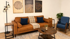 Ein Wohnzimmer mit einem braunen Sofa, blauen Sesseln, einem Couchtisch und drei gerahmten Kunstwerken an der Wand.