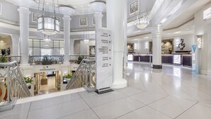 Un hallo espacioso con techo alto, varios candelabros y una columna central con señalización.